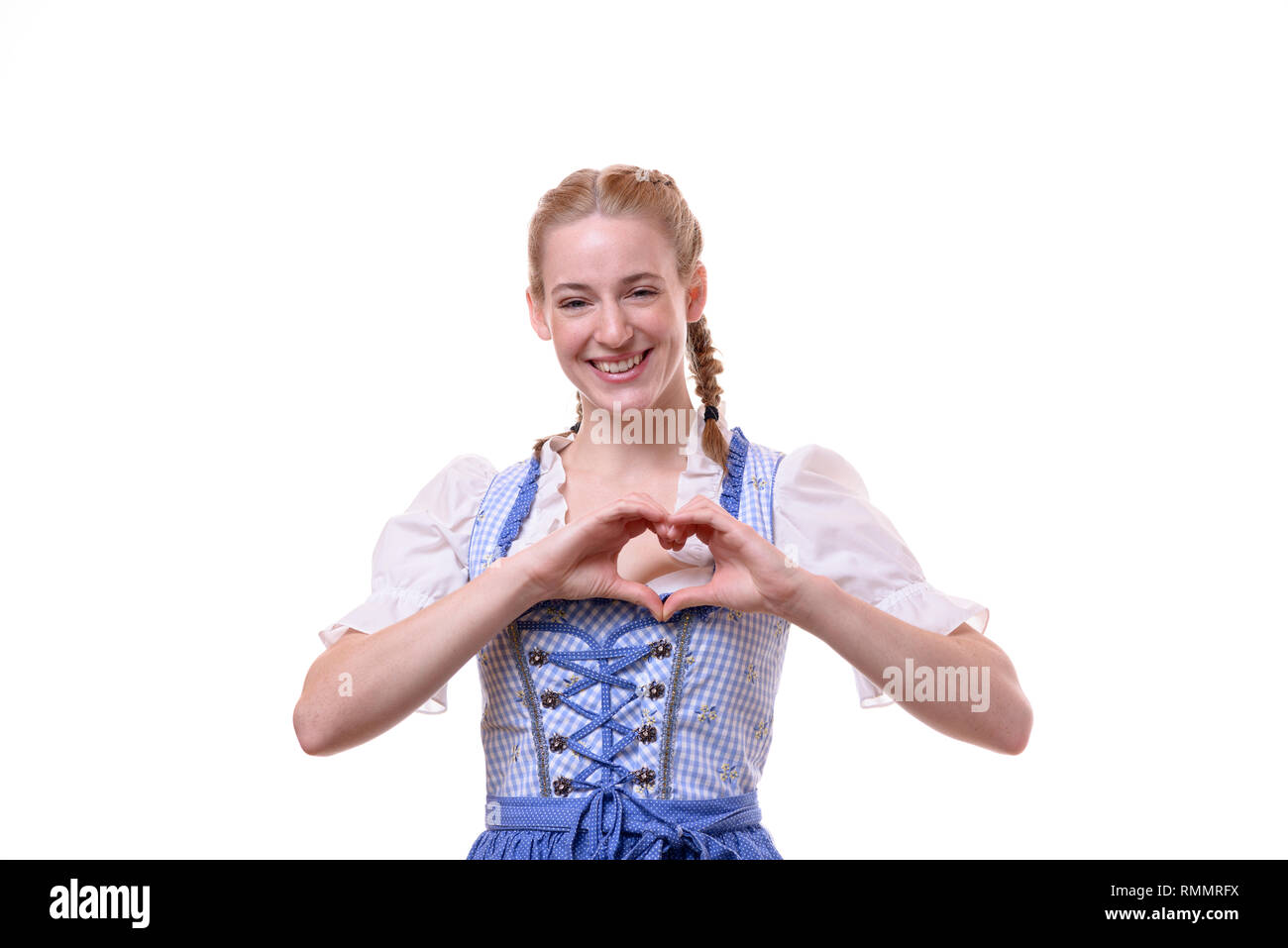 Studio shot portrait of a beautiful German young woman wearing traditional Bavarian dress for Oktoberfest while smiling and making a heart shape with  Stock Photo