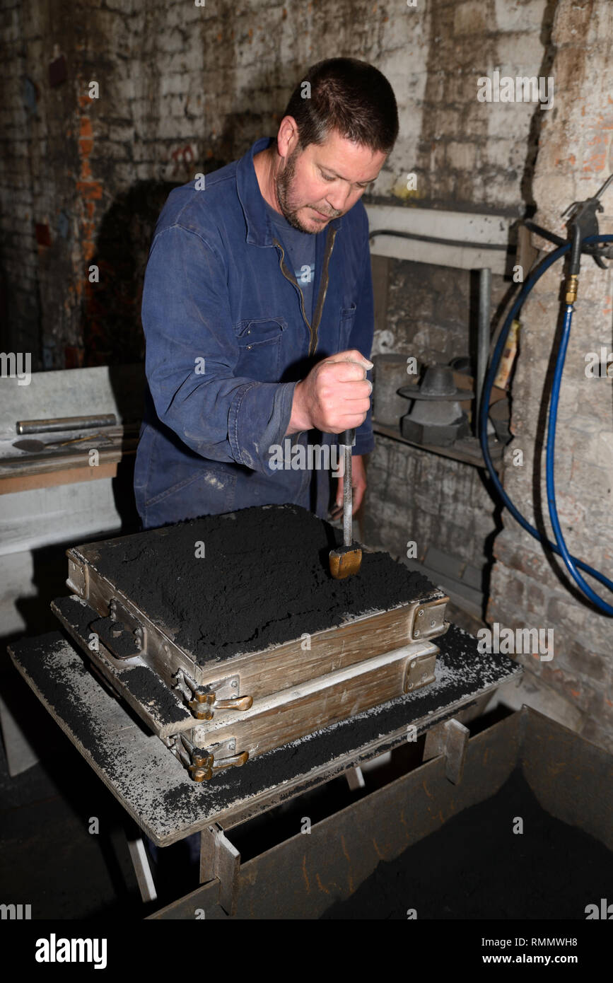A foundryman pounds wet sand into a mould for making a fire grate from molten iron Stock Photo