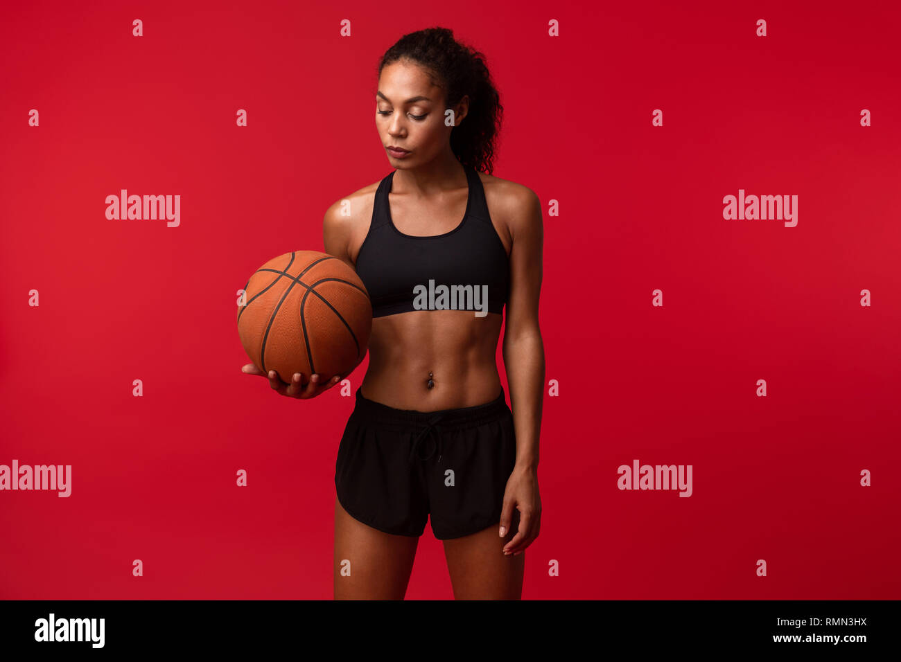 Image of a strong young african sports fitness woman basketball player posing isolated over red wall background holding ball. Stock Photo