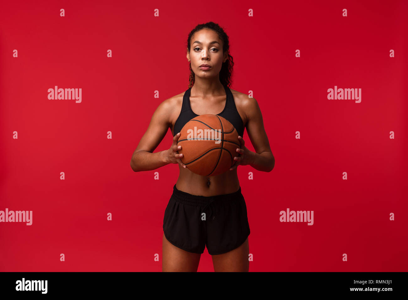 Image of a strong young african sports fitness woman basketball player posing isolated over red wall background holding ball. Stock Photo