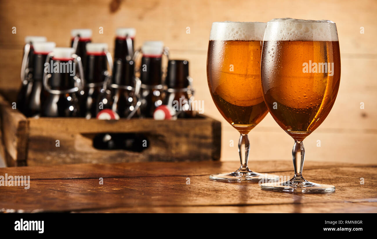 Two glasses of chilled beer with frothy heads standing together on a