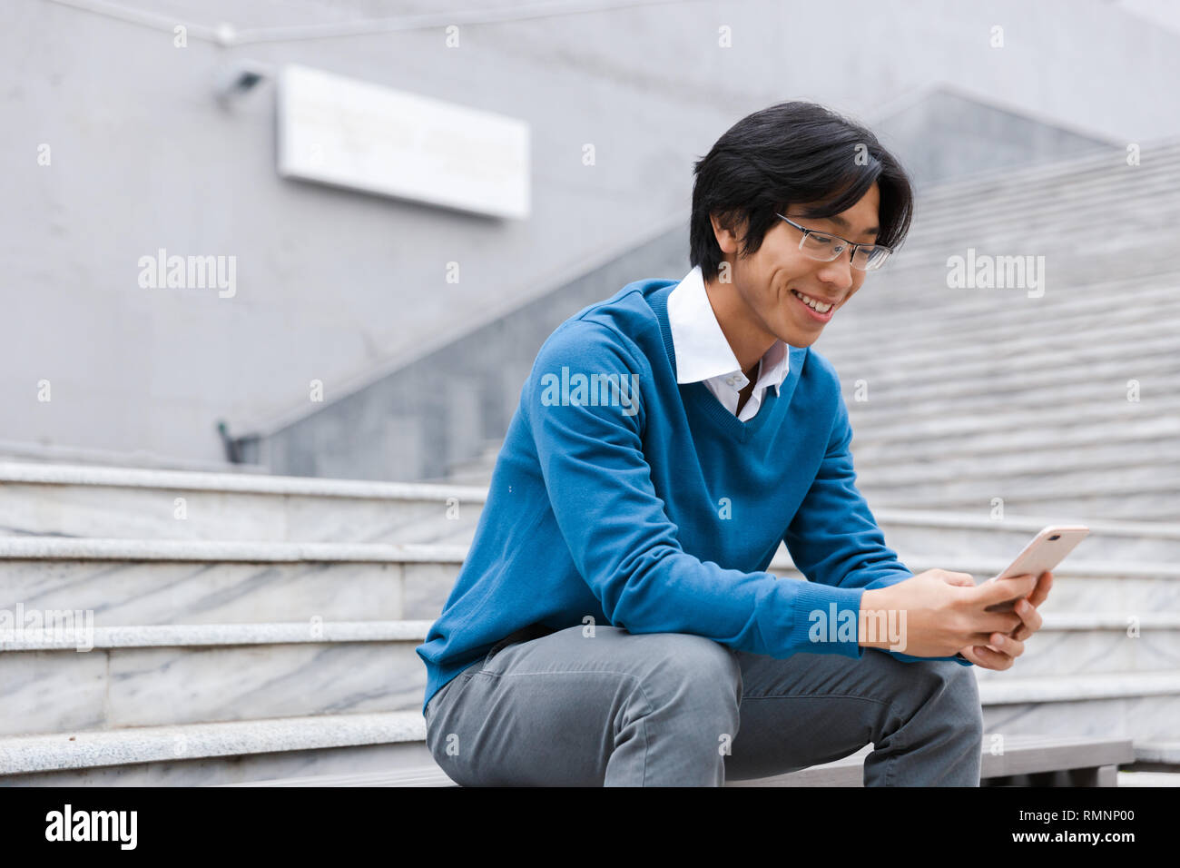 Smiling young asian man talking on mobile phone while sitting on the ...