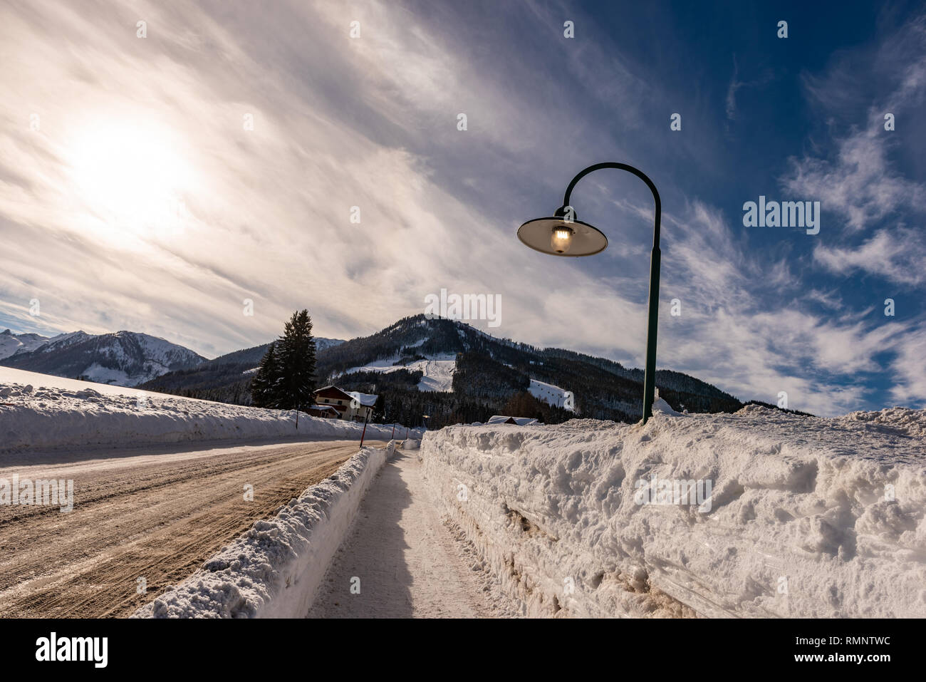 Street lamp on during the day on a snowy, empty street in winter. Sun and mountains background. Rohrmoos Untertal Schladming Dachstein, Austria Europe Stock Photo