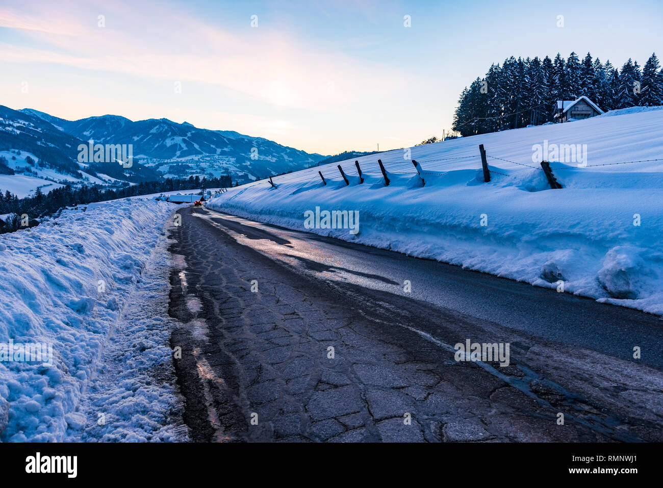 Empty, asphalt, destroyed road in winter. Big snow around and snow-covered mountains at sunset. Birnberg, Schladming Dachstein, Austria, Europe Stock Photo