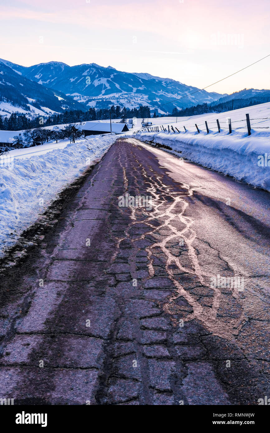 Empty, asphalt, destroyed road in winter. Big snow around and snow-covered mountains at sunset. Birnberg, Schladming Dachstein, Austria, Europe Stock Photo