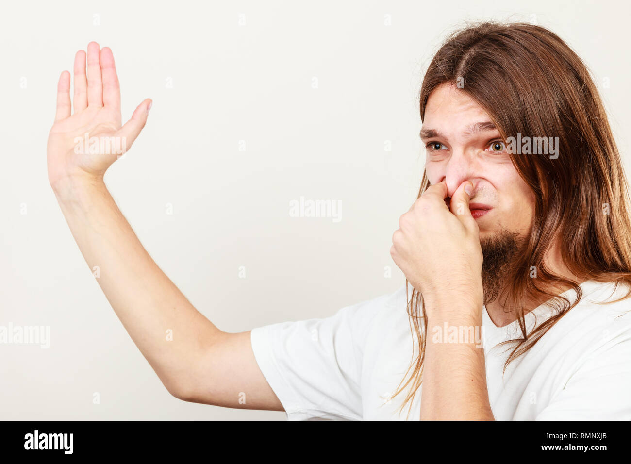 Expression of very bad smell. Young long haired sweaty man making hand