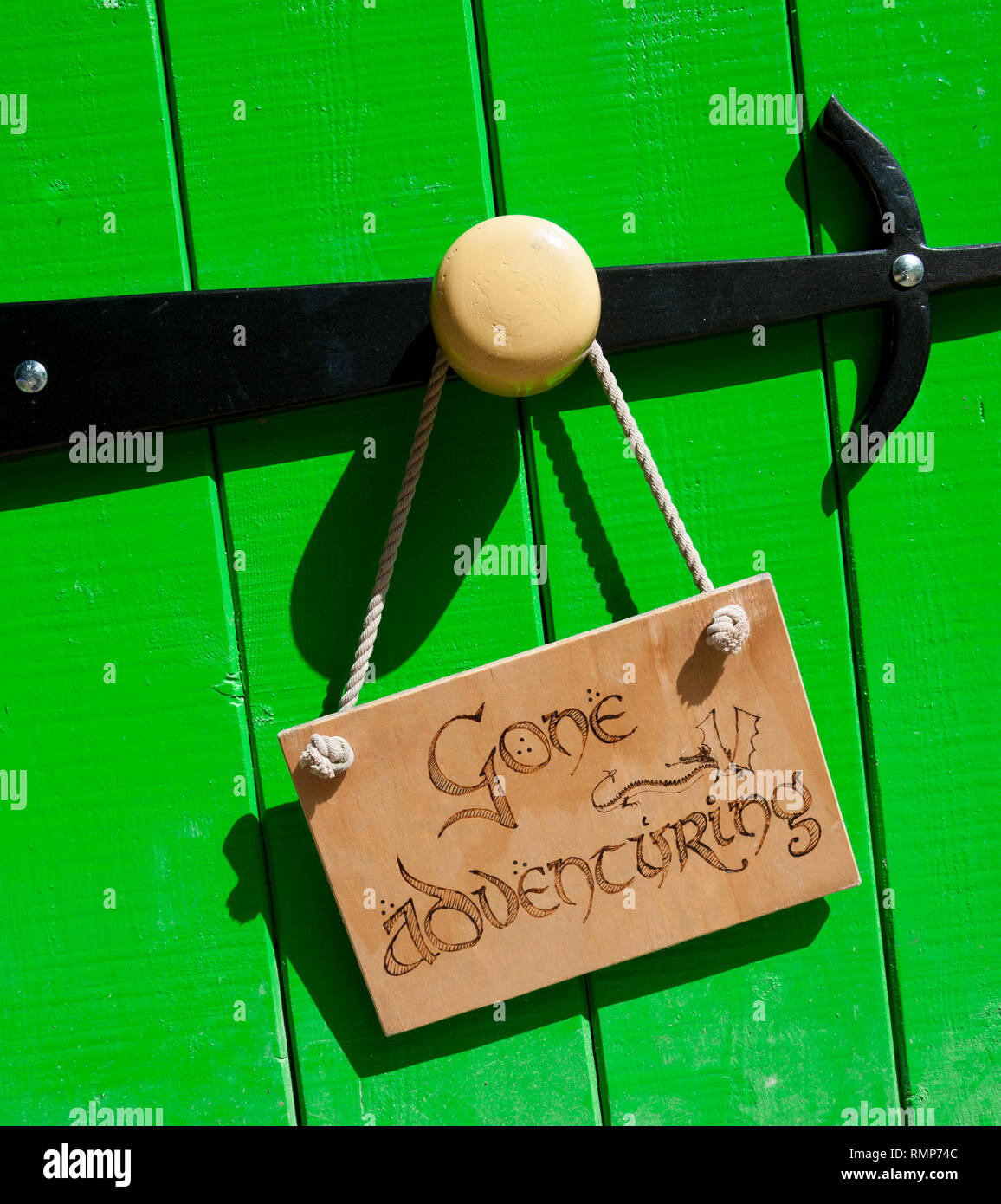 Green wooden door with large round knob and black hinge.  Gone Adventuring sign hung from door knob Stock Photo