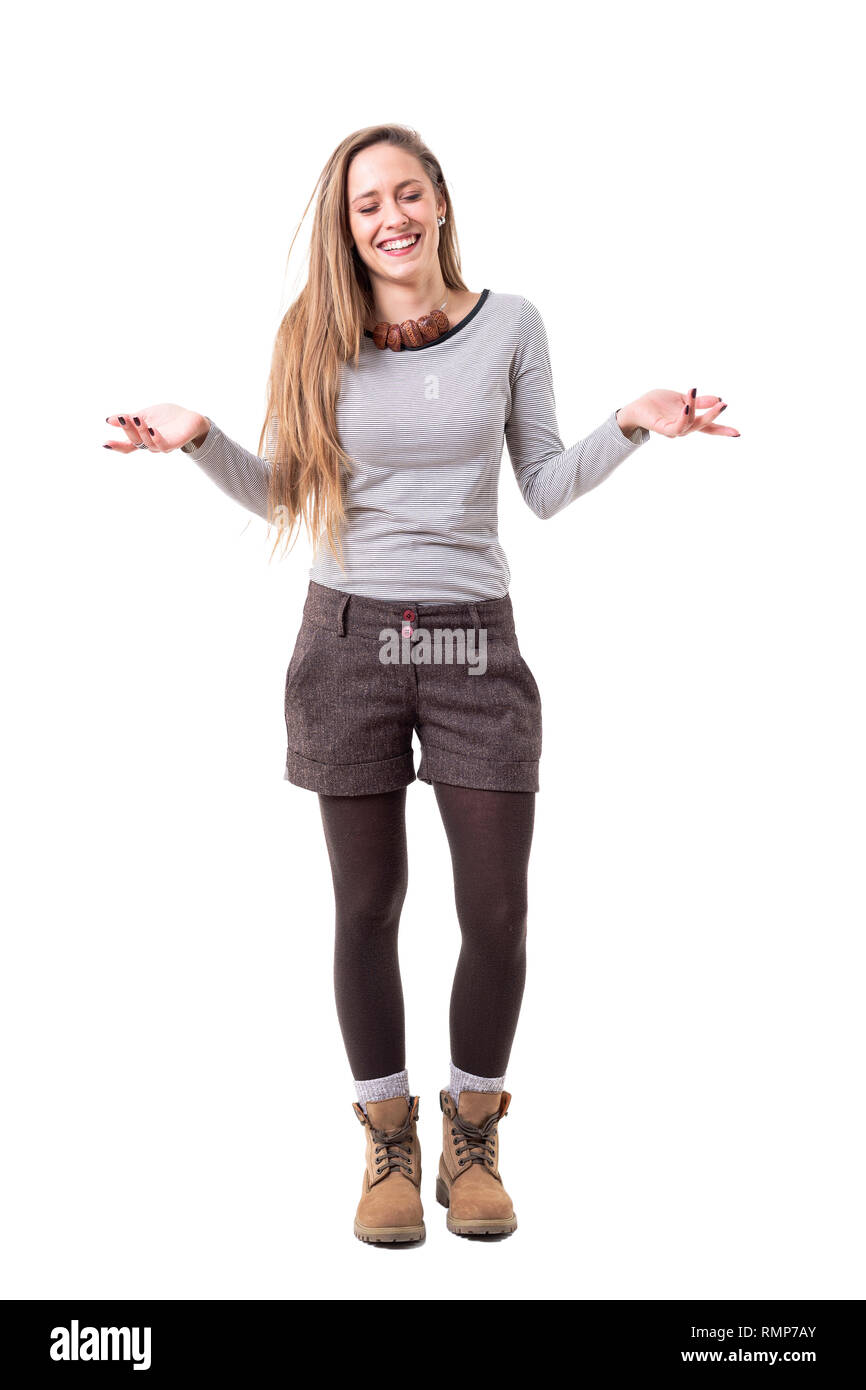 Pretty young confused and clueless woman laughing with closed eyes while shrugging shoulders. Full body isolated on white background. Stock Photo