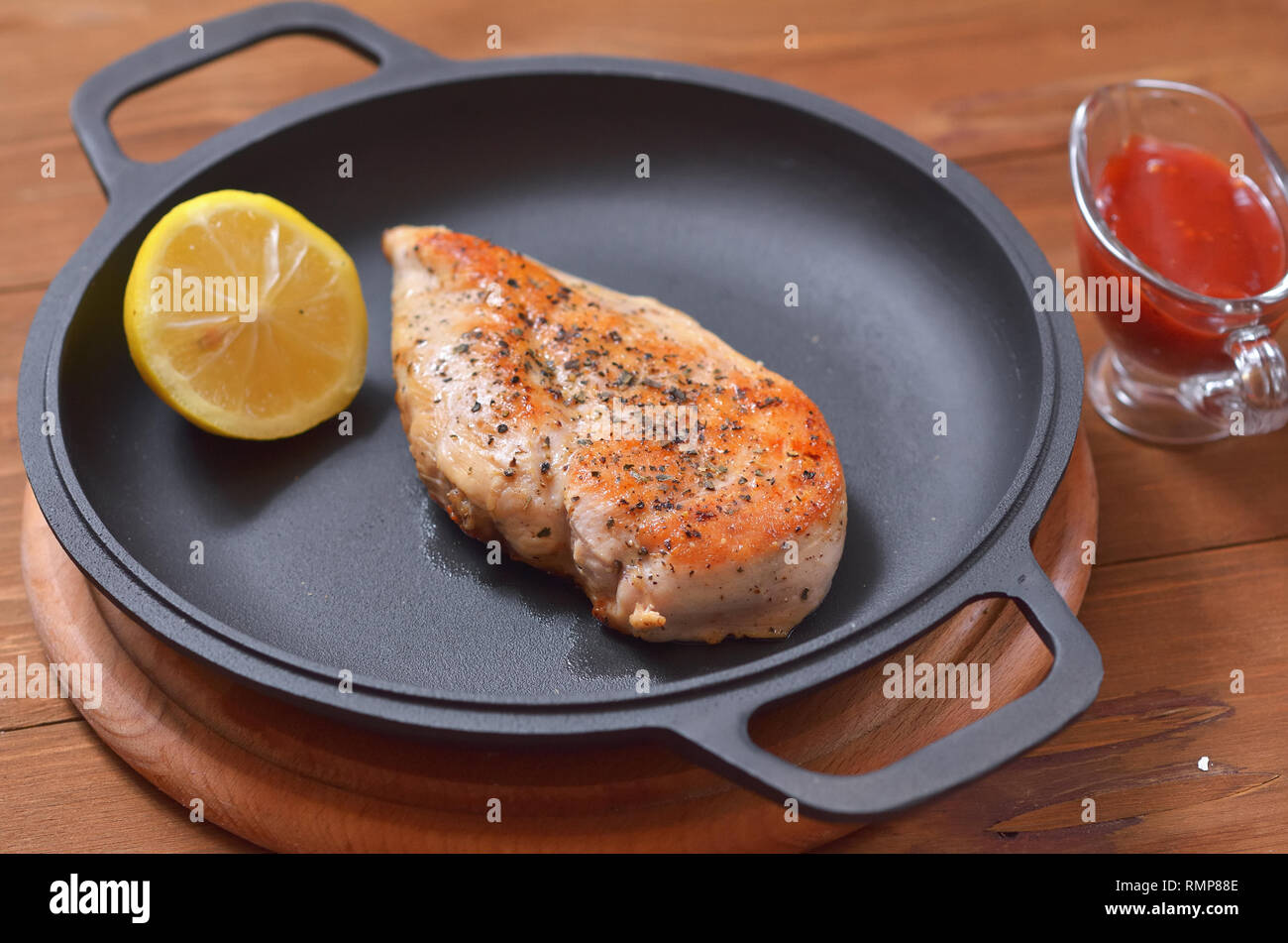 Large chicken fillet with lemon fried in a pan, next to the table there