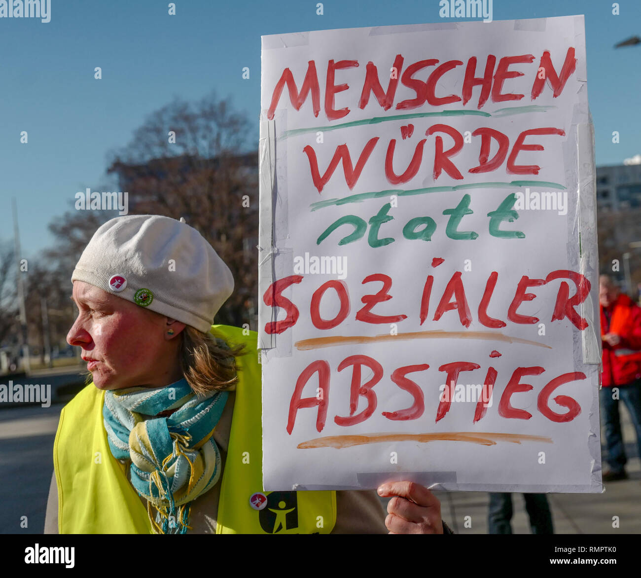 Dresden, Germany. 16th Feb, 2019. A woman with a warning vest and a poster with the inscription 'Human dignity instead of social decline' is standing at the demonstration of the collection movement 'Aufstehen - Die Sammlungsbewegung' at one of the nationwide rallies in Dresden. The demonstrators are called upon to appear in colourful warning vests, modelled on the French yellow vests. Demonstrations were announced in at least 14 German cities. Credit: Peter Endig/dpa/Alamy Live News Stock Photo