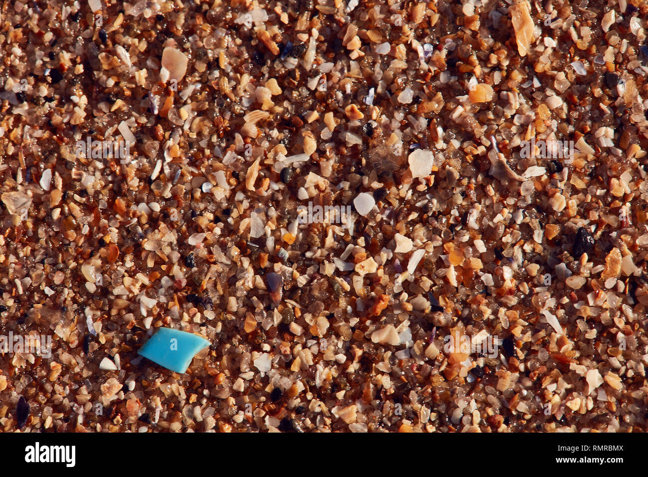 single micro plastic nurdle, blue, on sand Stock Photo