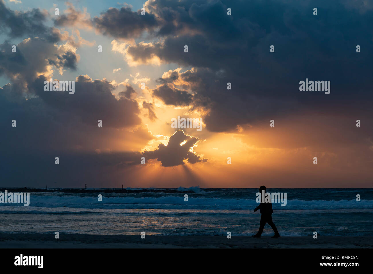 A silhouette of a man waking on the beach in sunset time, photographed in Tel Aviv, Israel Stock Photo
