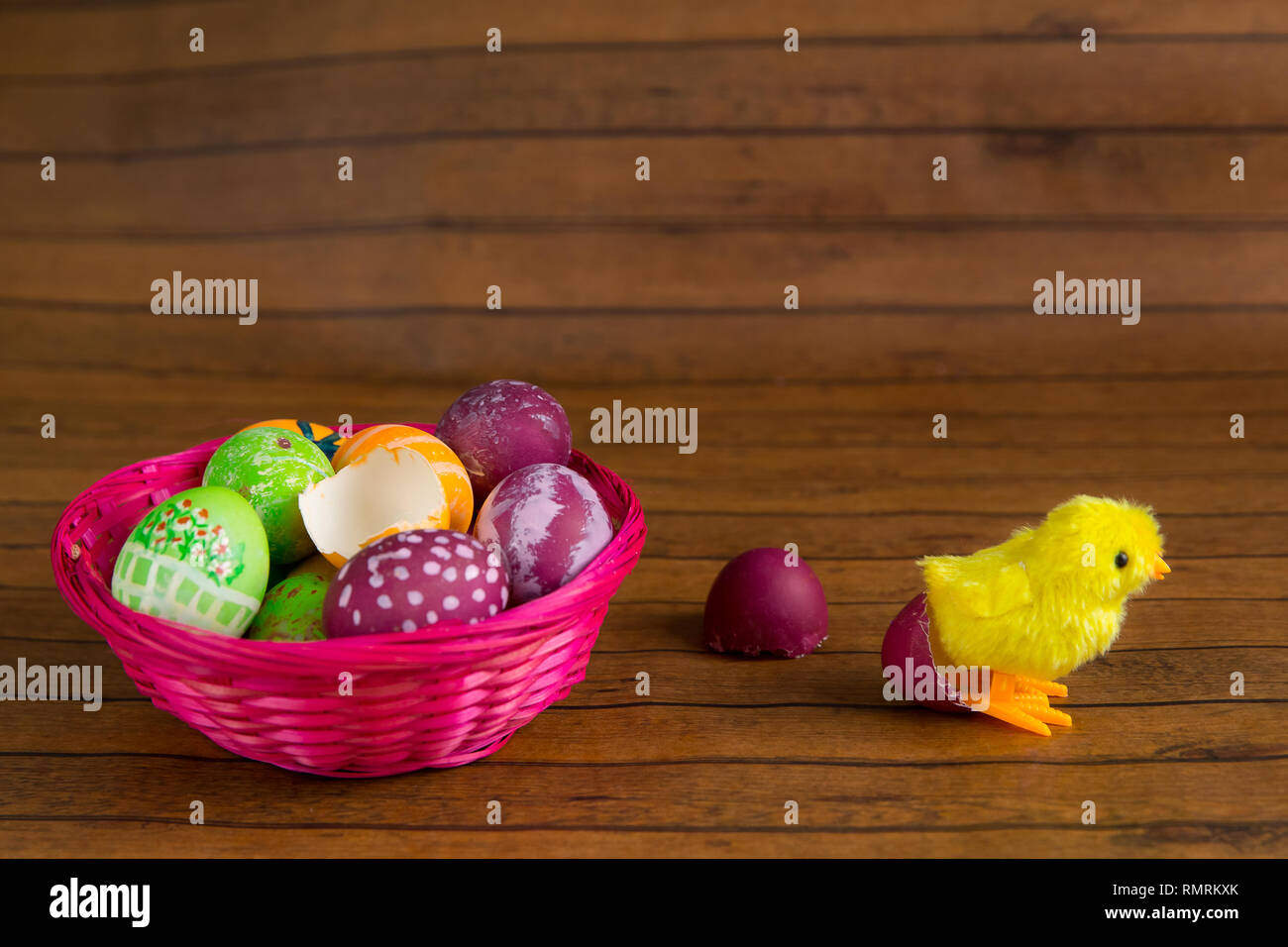 Easter Color Painted Eggs In Basket And Toy Chick On Wooden Table