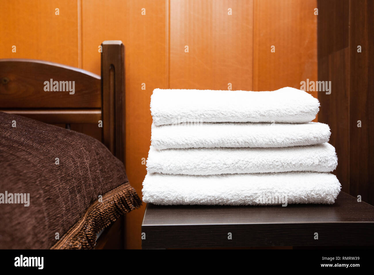 A stack of clean white towels lies on a bedside table in a hotel room