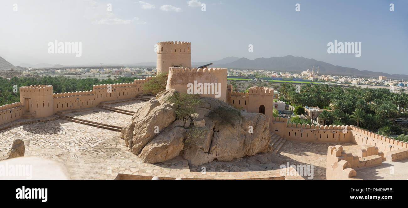 Walls and turrets of the Fort of Nahkal and the village with the mosque in the background (Oman) Stock Photo