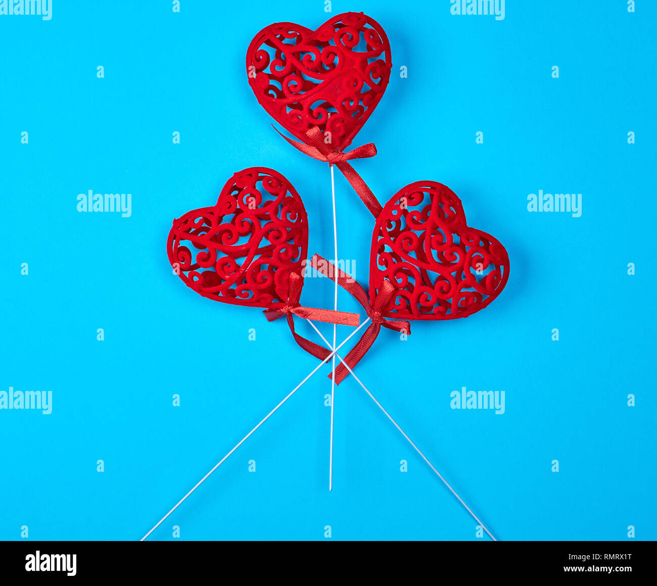 three red carved hearts on a stick on a blue background Stock Photo