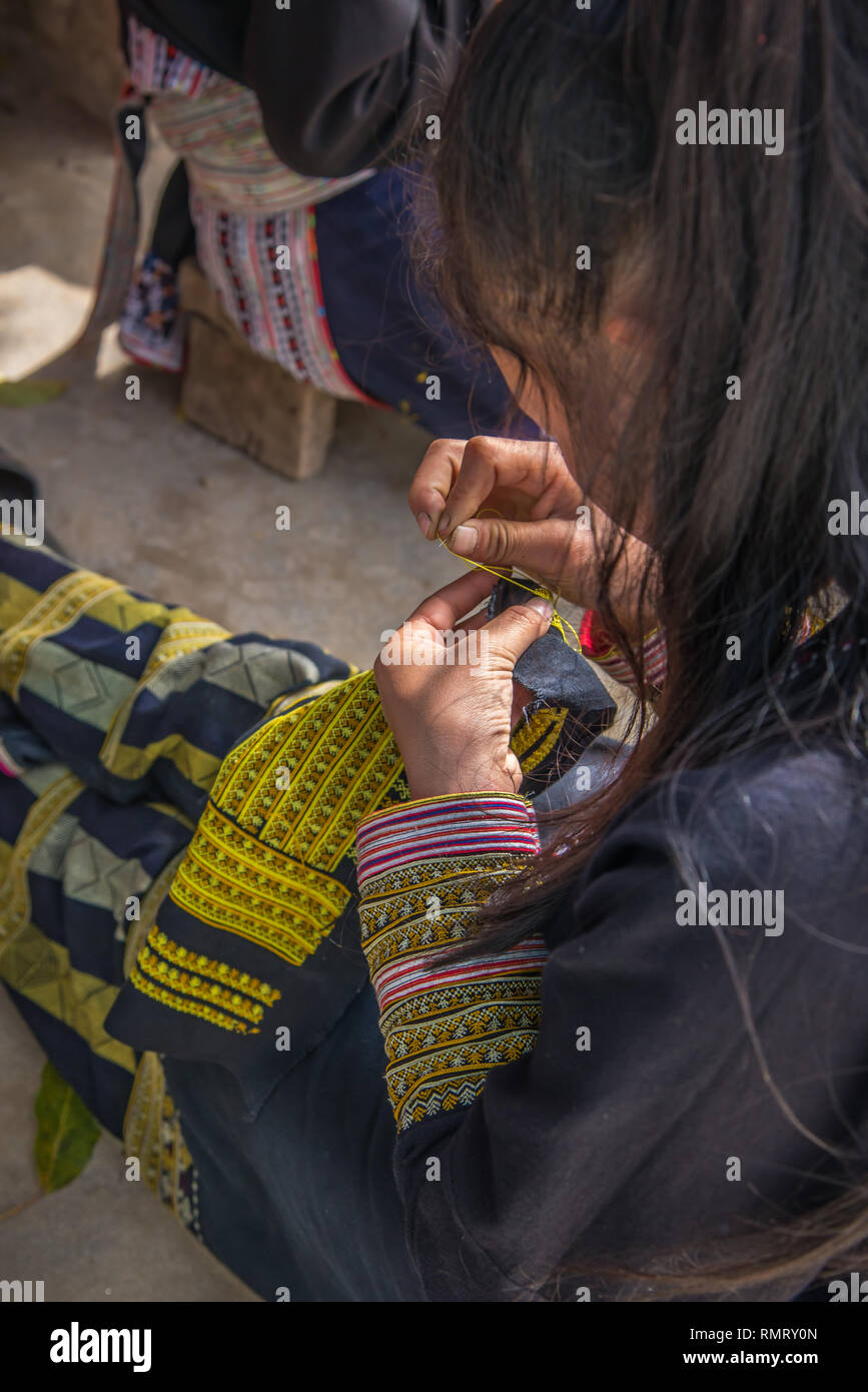 Vertical close-up of a Red Dao woman creating traditional embroidery patterns in yellow thread on blue fabric in Ta Phin near Sapa, Vietnam. Stock Photo