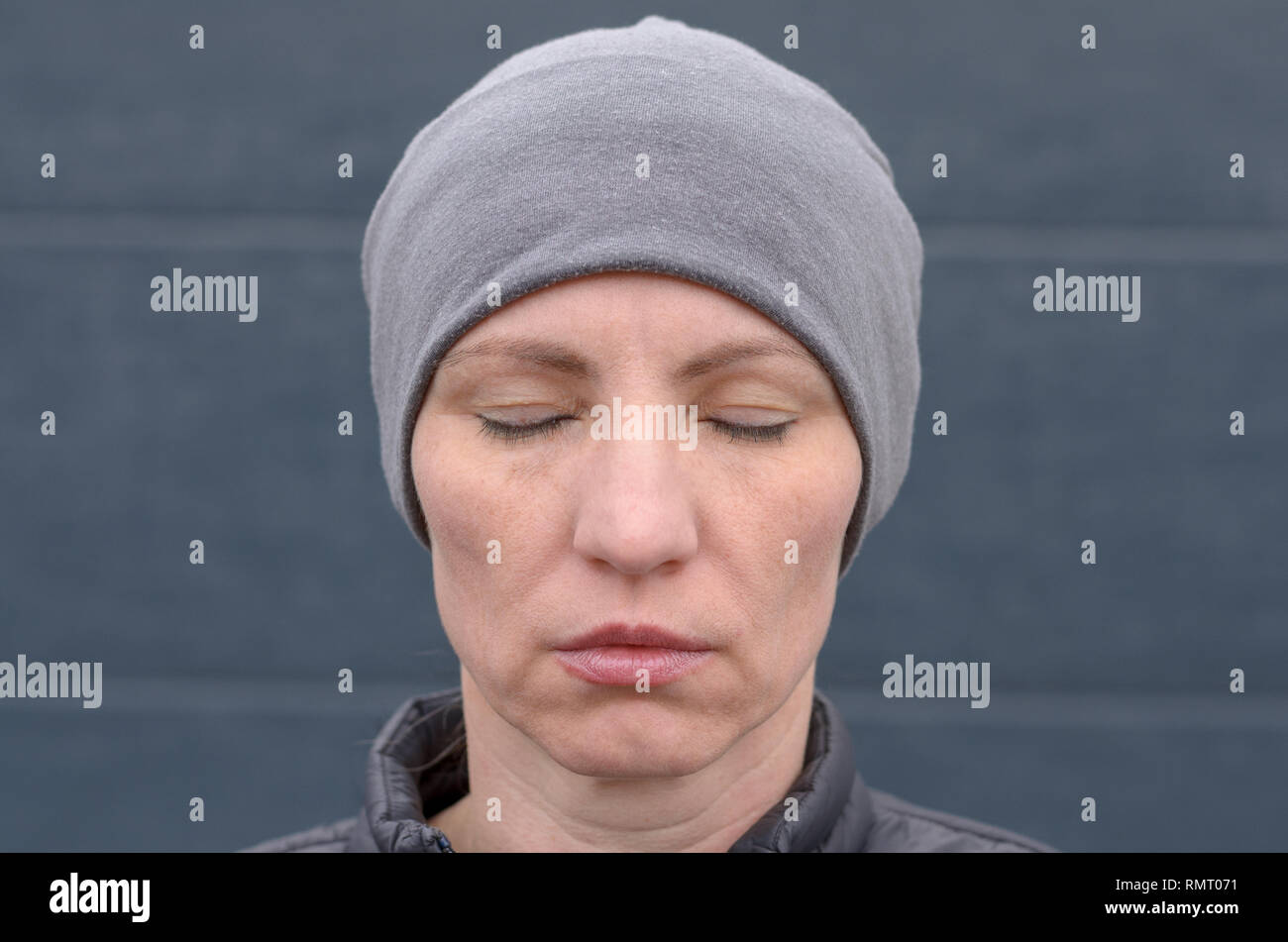 Calm unemotional woman wearing a grey knitted cap with closed eyes and a serene expression in a close up head shot Stock Photo