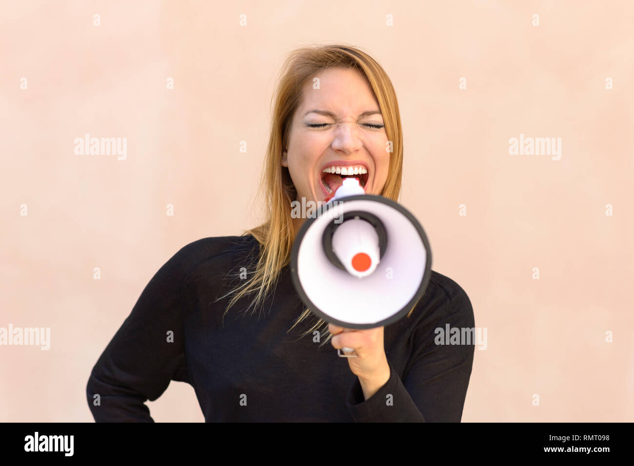 Angry woman airing her grievances yelling into a megaphone or bullhorn at a demonstration or protest in a frontal view Stock Photo