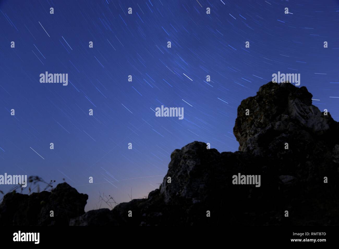 Star trails representing rotation of celestial sphere with rocks on a foreground. Stock Photo