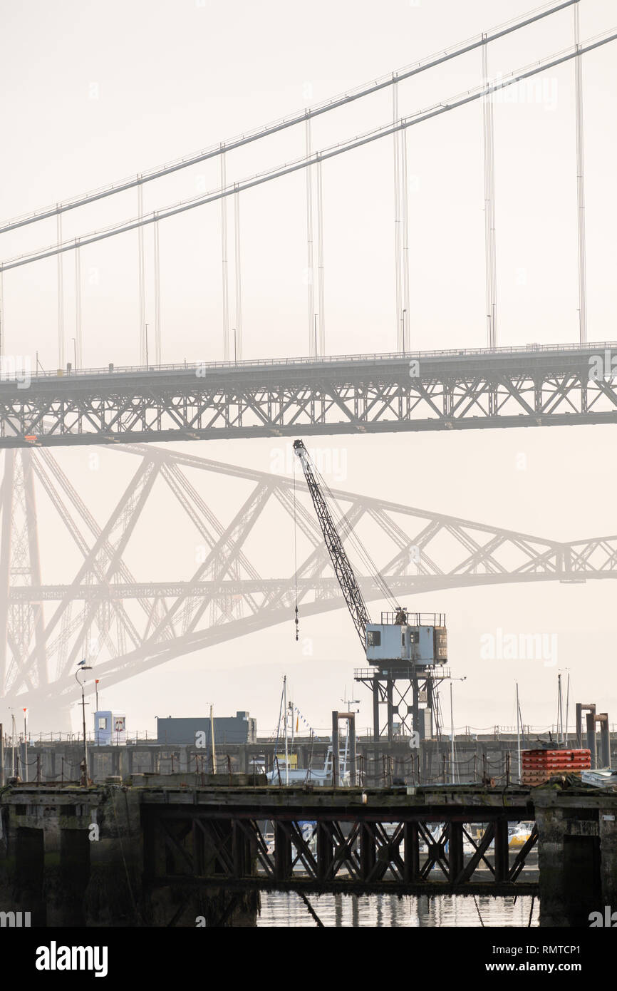 The old Forth Road bridge with a crane in the foreground, and the Forth Railway Bridge in the background on a misty day, Queensferry, Scotland Stock Photo