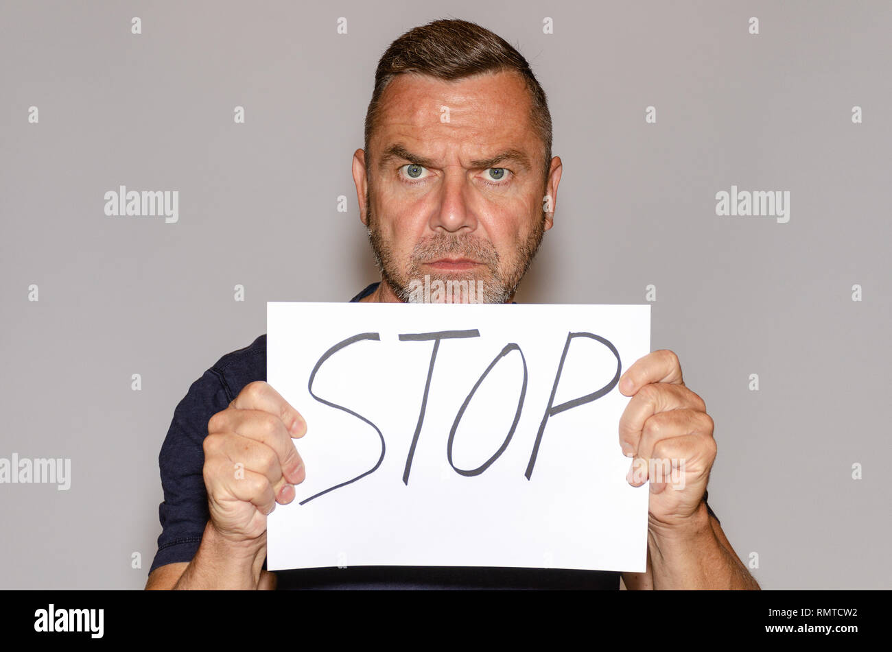 Stern implacable middle-aged man holding a handwritten Stop sign in ...