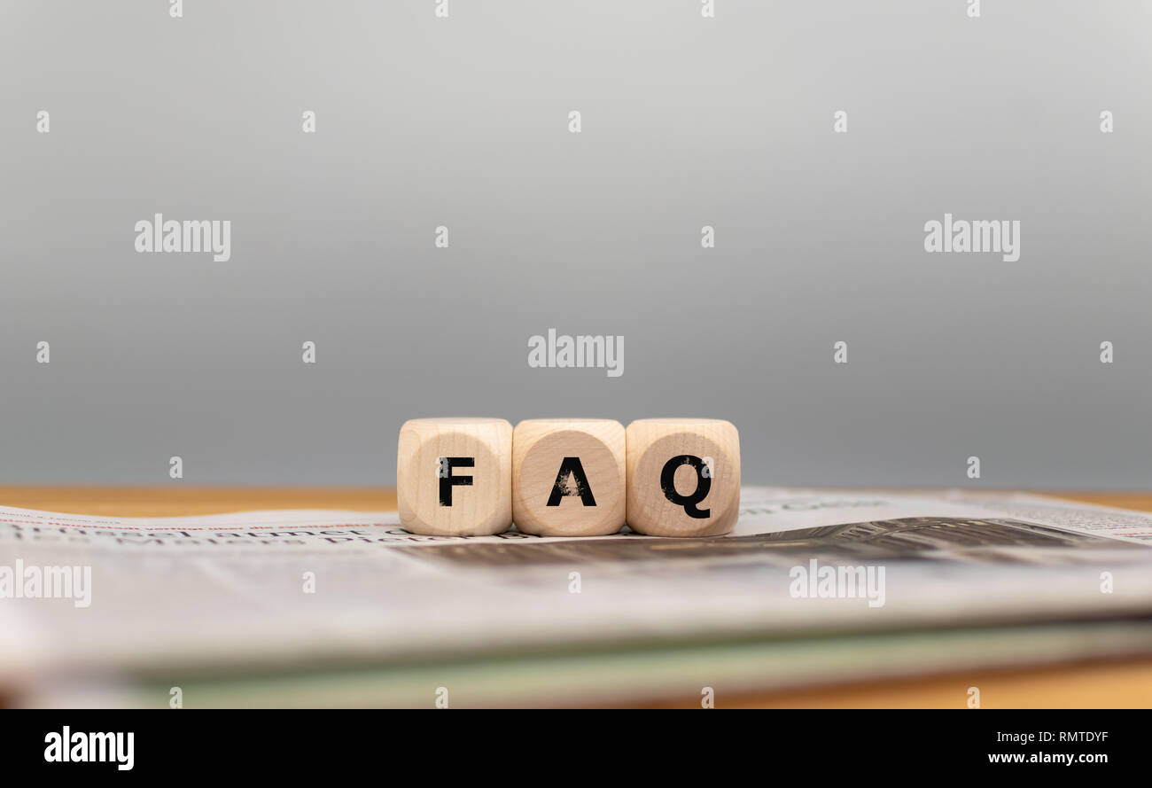 Dice form the acronym "FAQ" on a newspaper in front of a grey