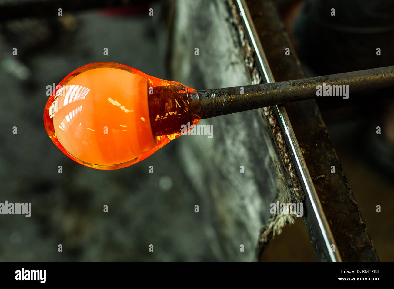 Glassblower man working with hot ocher glass to make a blown glass