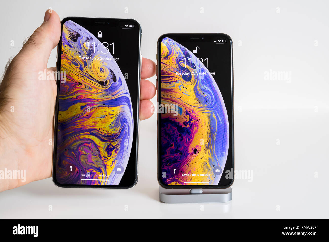 PARIS, FRANCE - SEP 25, 2018: Male hand compare new iPhone Xs and Xs Max  smartphone model by Apple Computers close up with home screen before  unlocking the device and liquid wallpaper