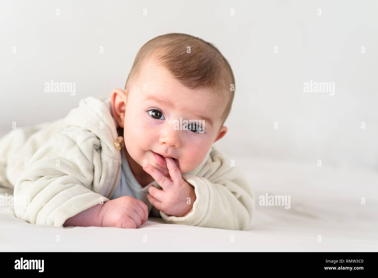 Portrait of an adorable smiling baby biting her own fingers putting her