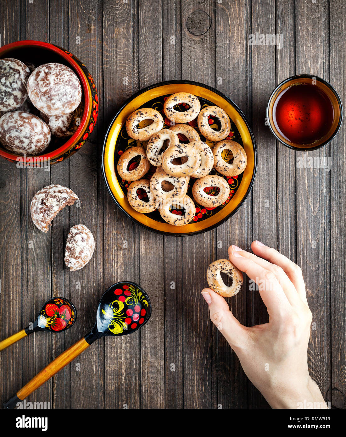 Table with Russian dessert sweet gingerbread and woman hand holding bublik biscuit, wooden spoon painted with floral ornament in the style of Khokhlom Stock Photo