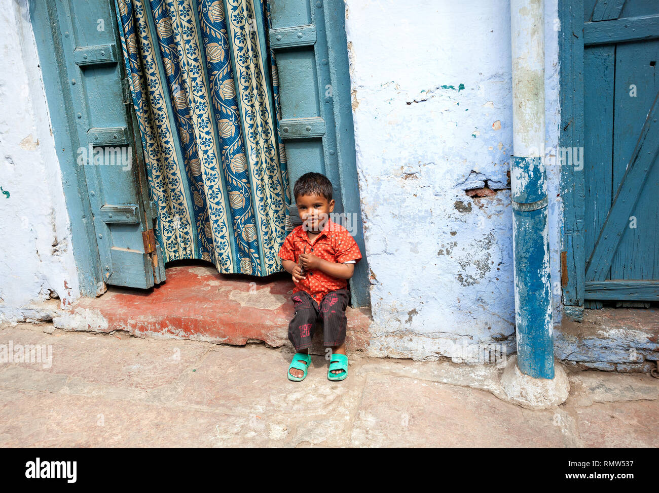 AGRA, UTTAR PRADESH, INDIA - FEBUARY 24, 2015: Small Indian boy sitting near his house door at narrow street of Taj Ganj district. Stock Photo