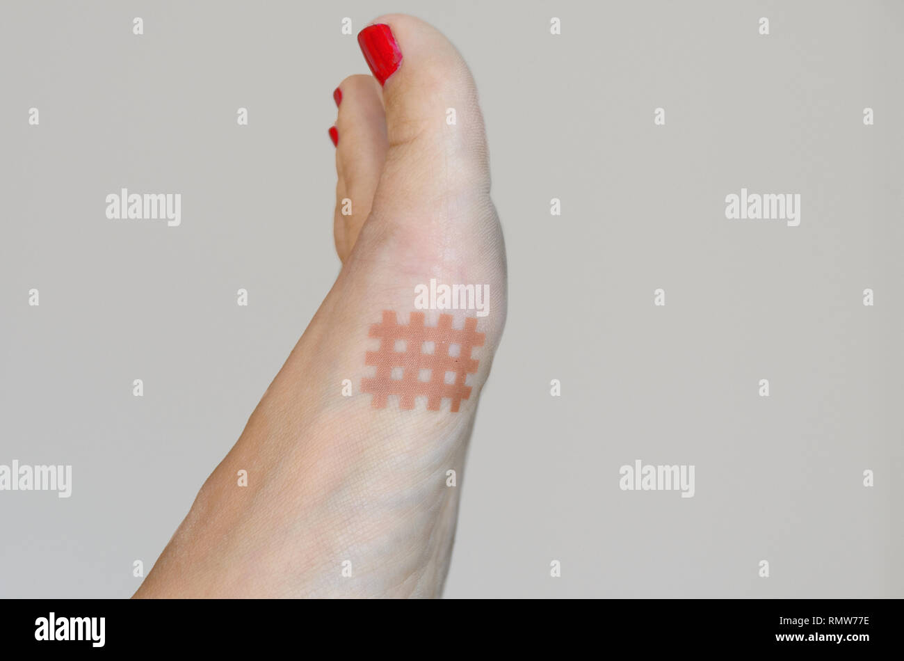 Skin colored lattice shaped tape stuck to women's foot with red nail
