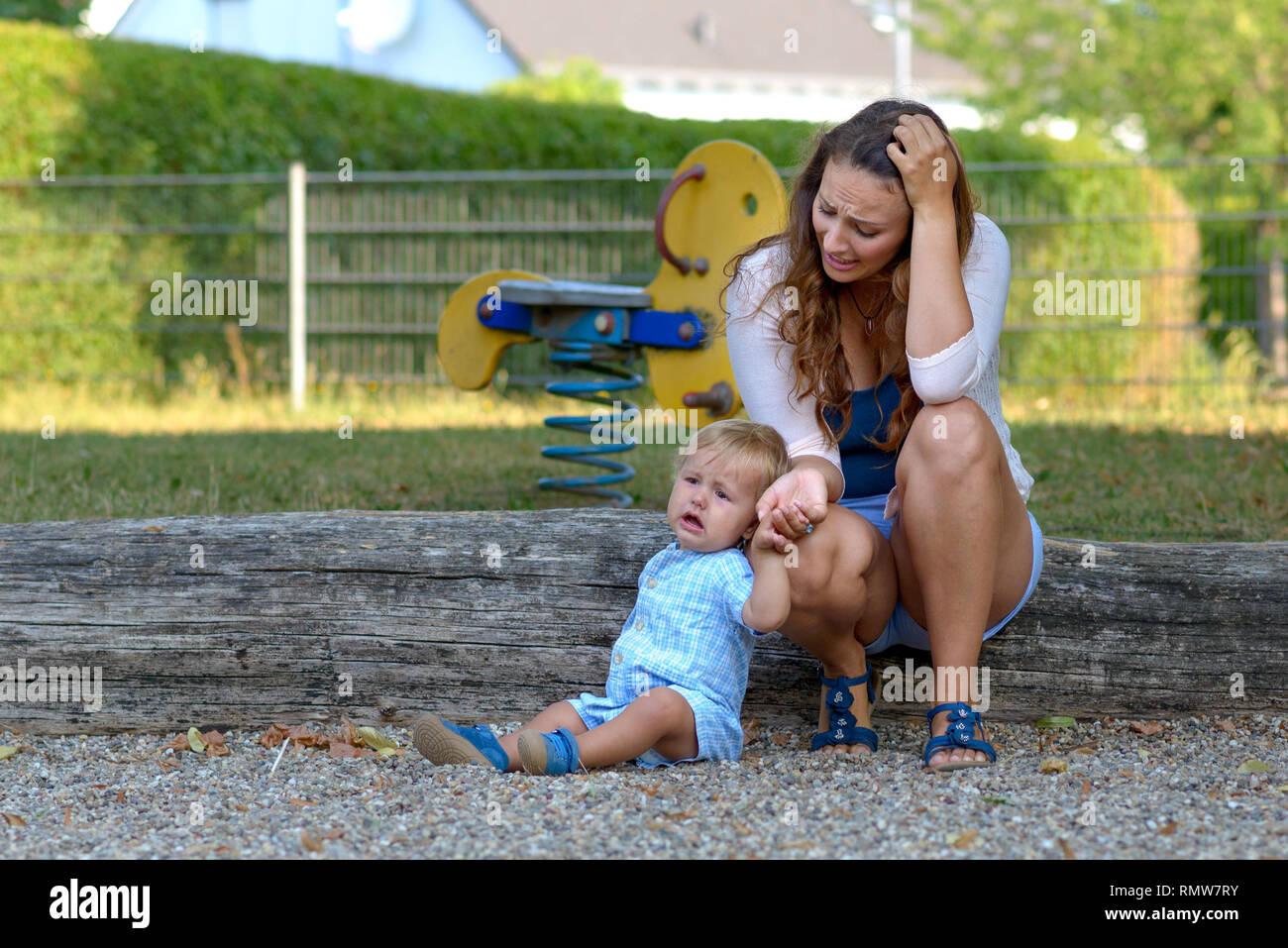 Troubled stressed young mother with her crying unhappy baby son outdoors in a playground Stock Photo