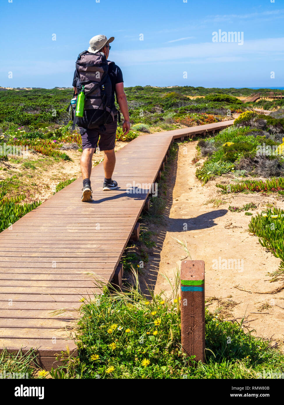 A hiker passes a striped signpost on the Fishermen's Trail between Zambujeira do Mar and Odeceixe in Portugal. The Fisherman's Trail is a four-day wal Stock Photo