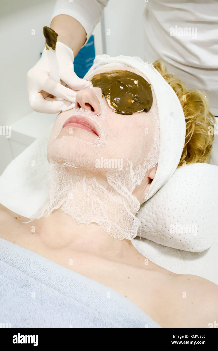 beautician worker applying cosmetic facial mask of sea algae for anti aging and hydration of skin to female client in beauty salon Stock Photo