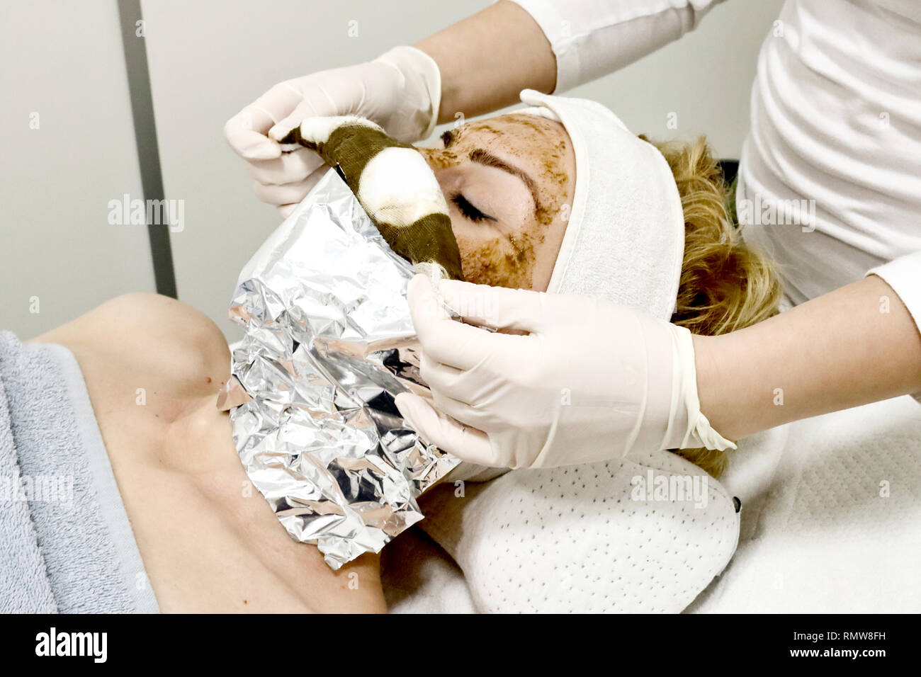 beautician worker removing  cosmetic facial mask of sea algae for anti aging and  hydration of skin  from female client in beauty salon close up Stock Photo