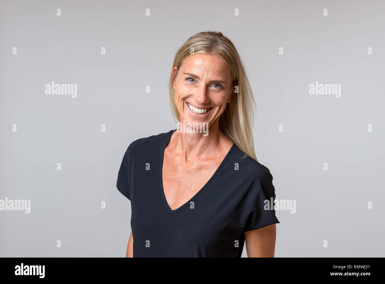 Attractive happy blond woman with a enthusiastic smile staring at the camera in a close up portrait isolated on grey Stock Photo