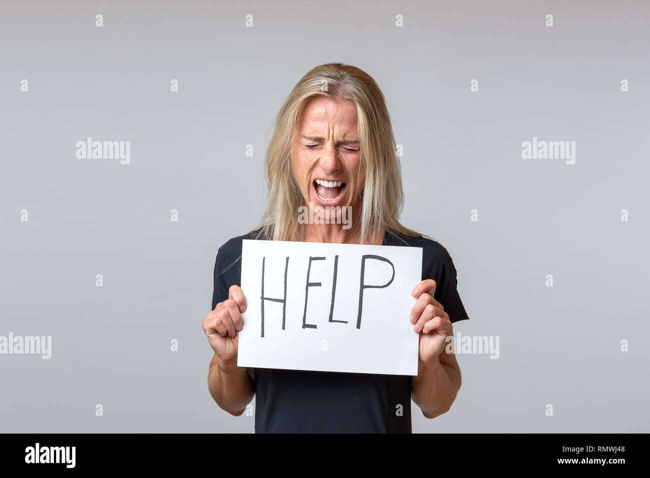 Desperate mature woman holding sheet of paper with help lettering against white background Stock Photo