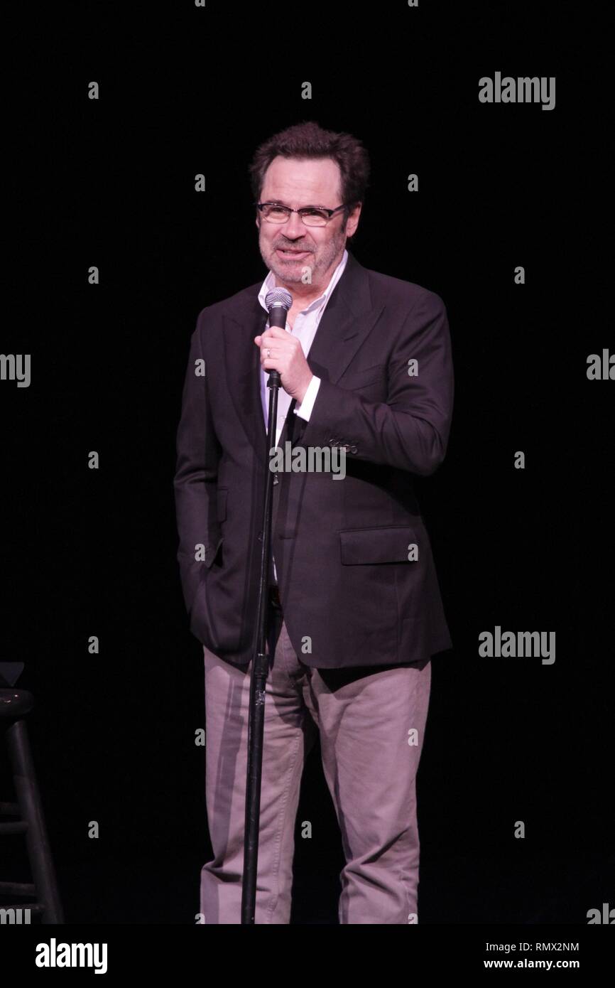 Comedian Dennis Miller is shown performing on stage during a "live
