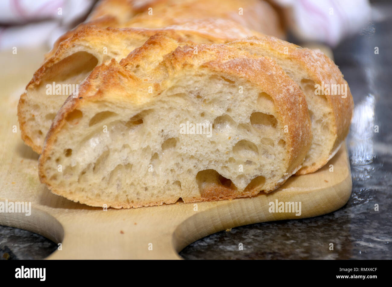 Sliced freshly baked crusty bread on a wooden bread board in a close up ...