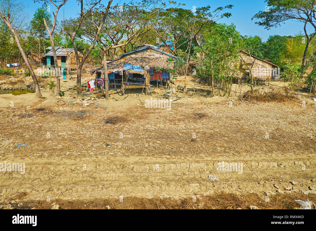 The shabby nipa huts on stilts among the green trees of the small forest, Dar Pein, Yangon suburb, Myanmar. Stock Photo