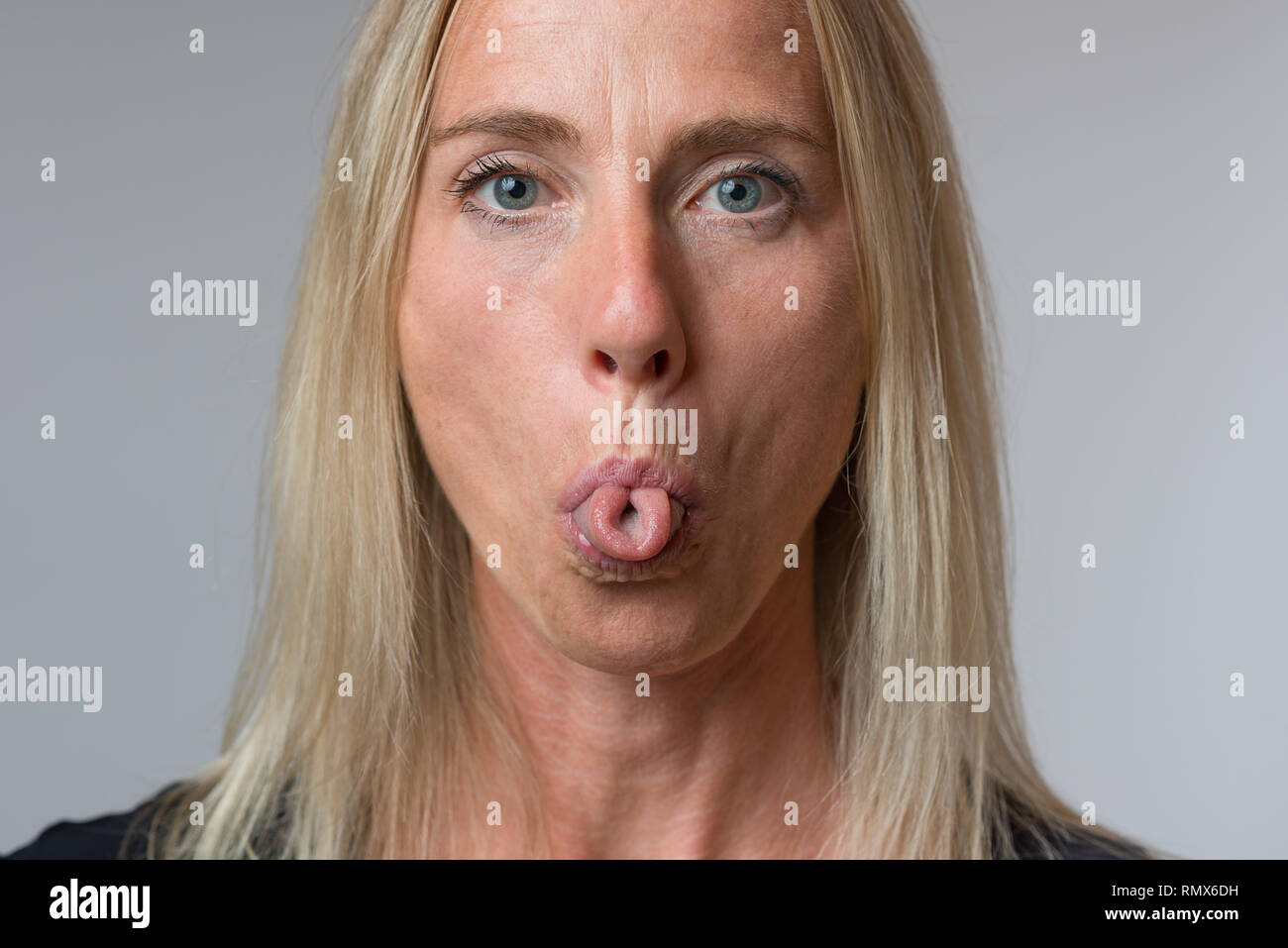 Mature woman sticking out her tongue at camera in a rude contemptuous gesture in a close up cropped face portrait Stock Photo