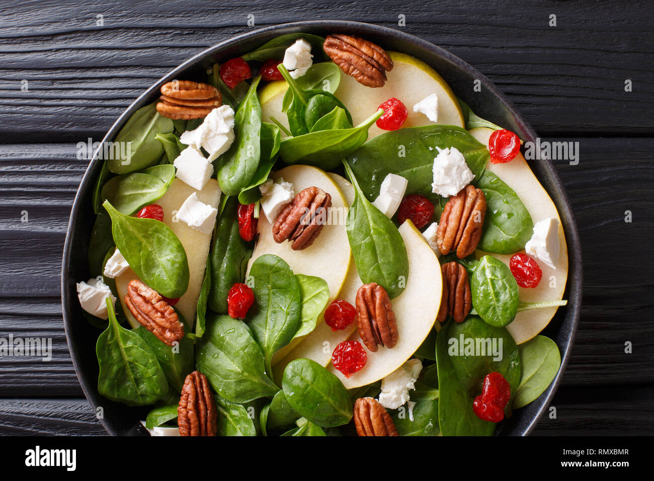 Spicy fruit salad with pears, baby spinach, pecans, feta cheese and cherries closeup on a plate on the table. horizontal top view from above Stock Photo