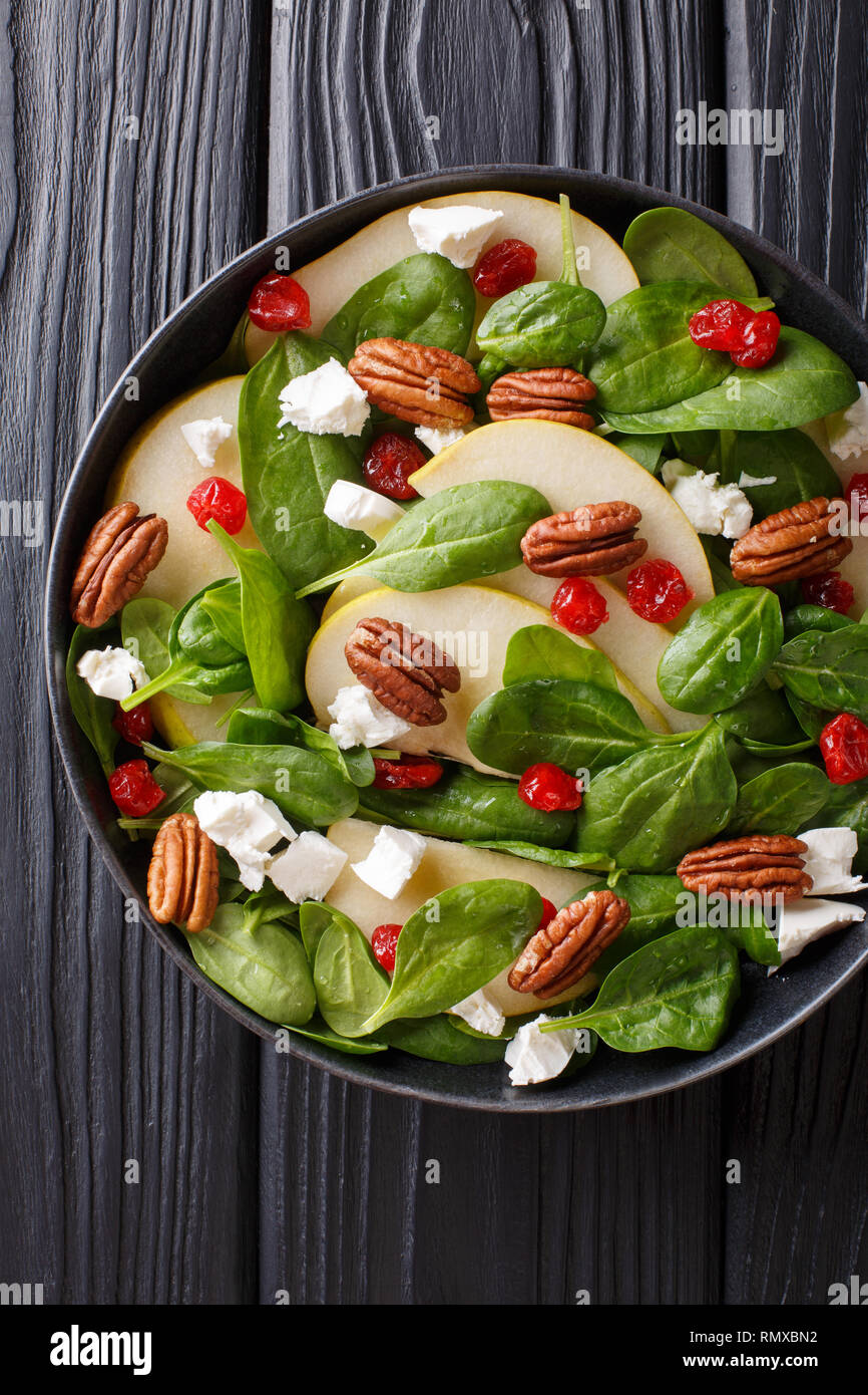 Spicy fruit salad with pears, baby spinach, pecans, feta cheese and cherries closeup on a plate on the table. Vertical top view from above Stock Photo