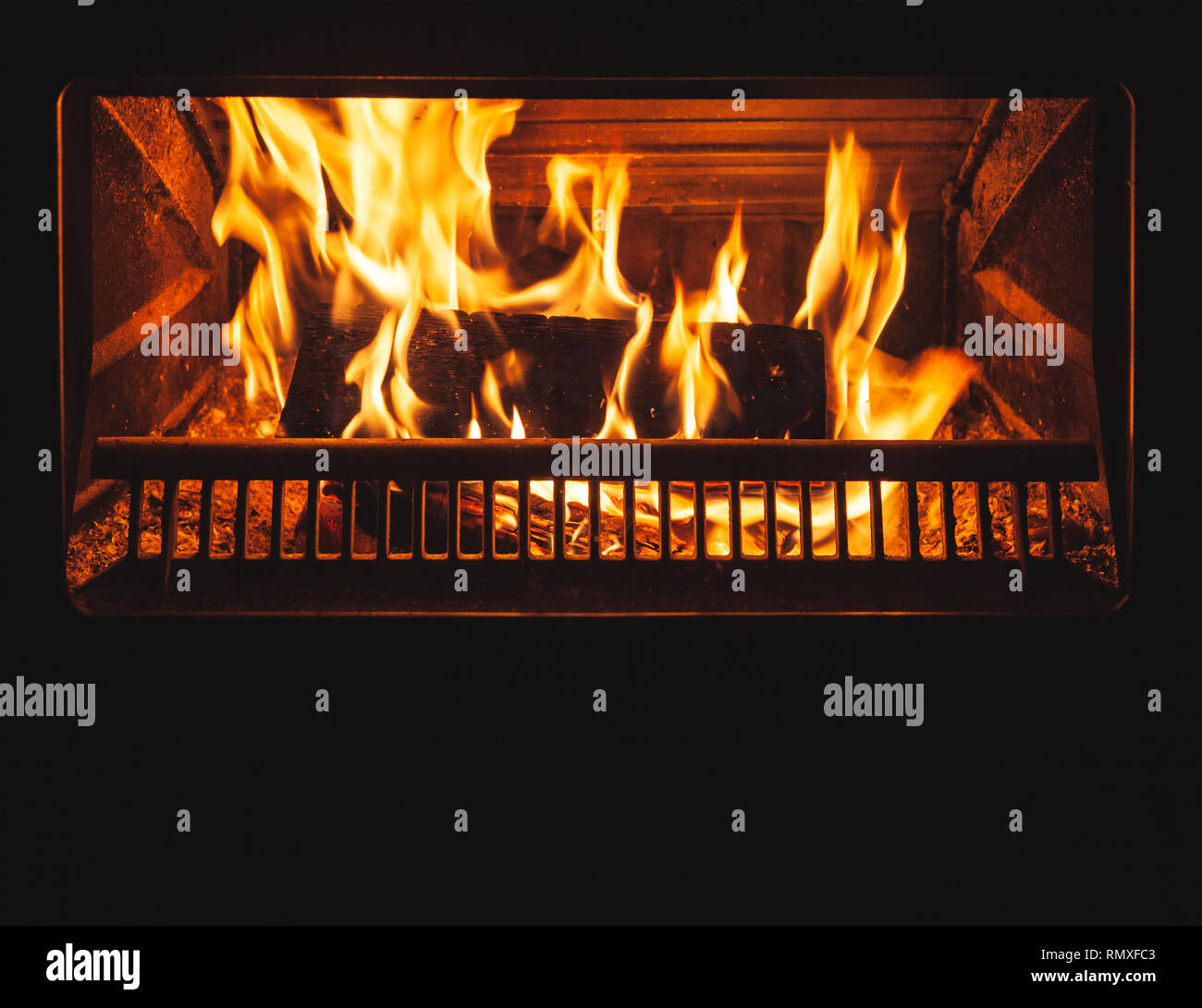 Firewood burns in the fireplace with a bright flame behind closed glass door Stock Photo