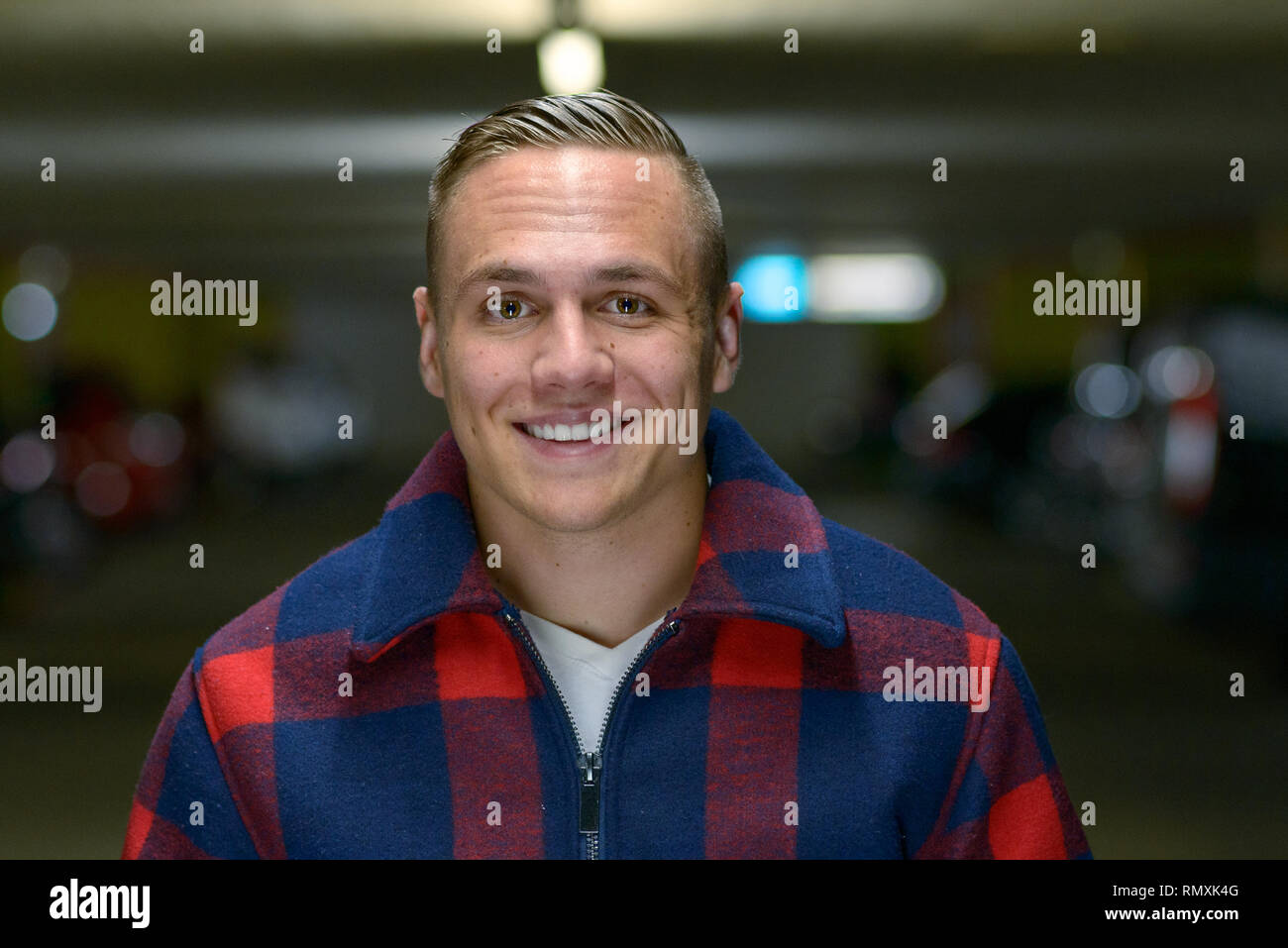 Portrait of a confident handsome and blond young man wearing a checkered jacket while smiling while looking at camera indoors Stock Photo