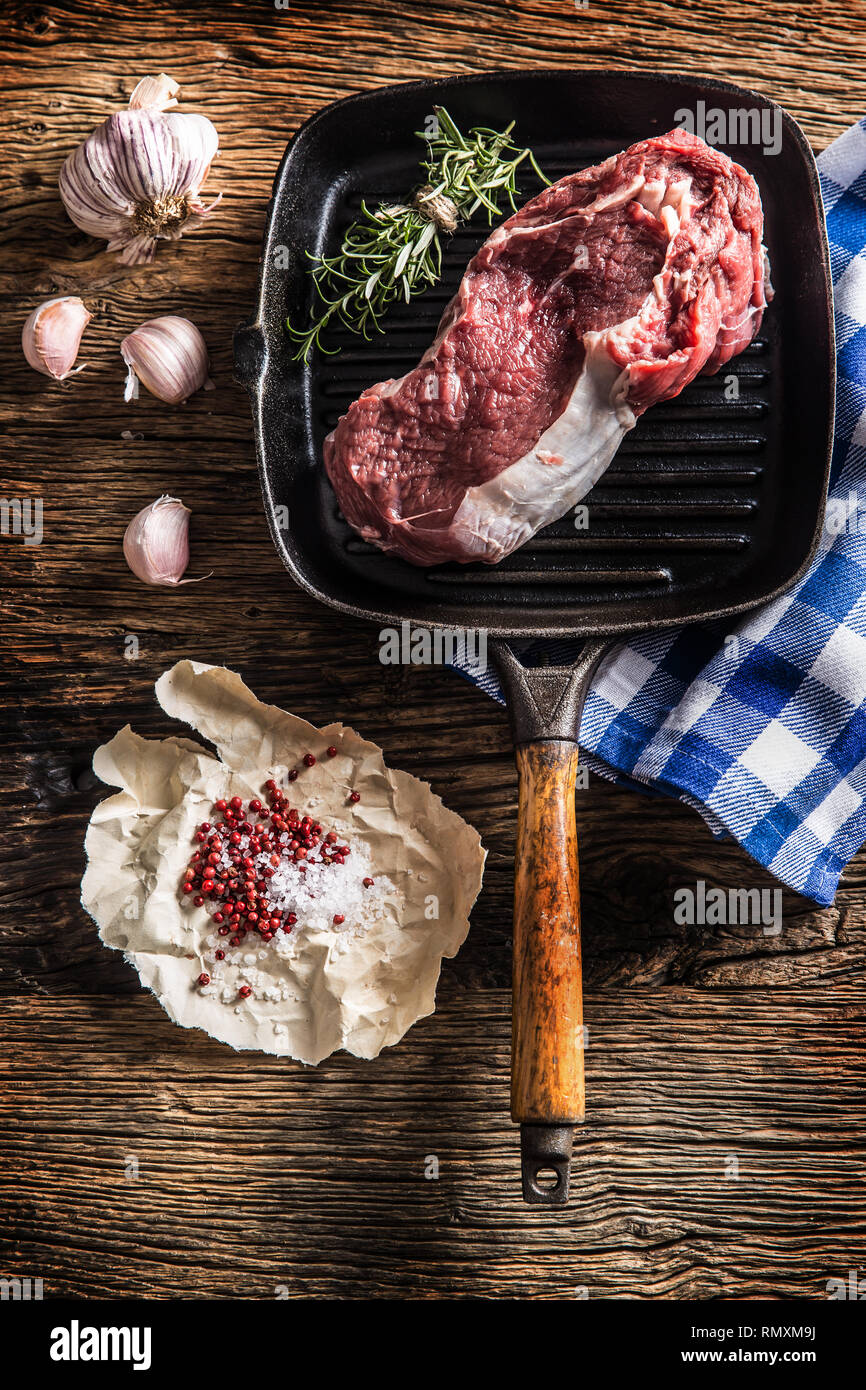 Raw beef steak in grill pan with salt pepper garlic and herbs on wooden
