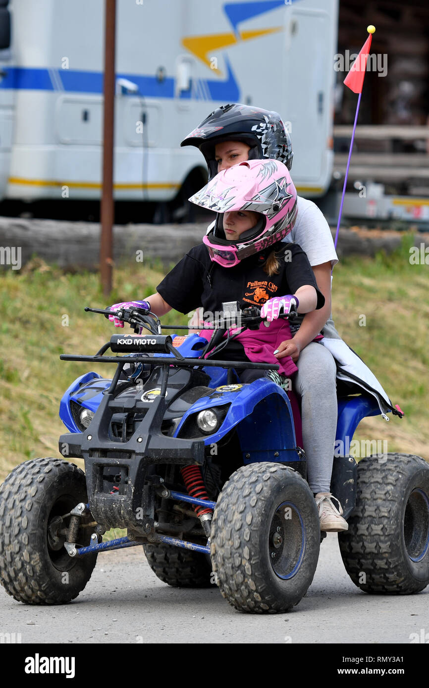 Two young females riding a small quad/ATV on the road Stock Photo