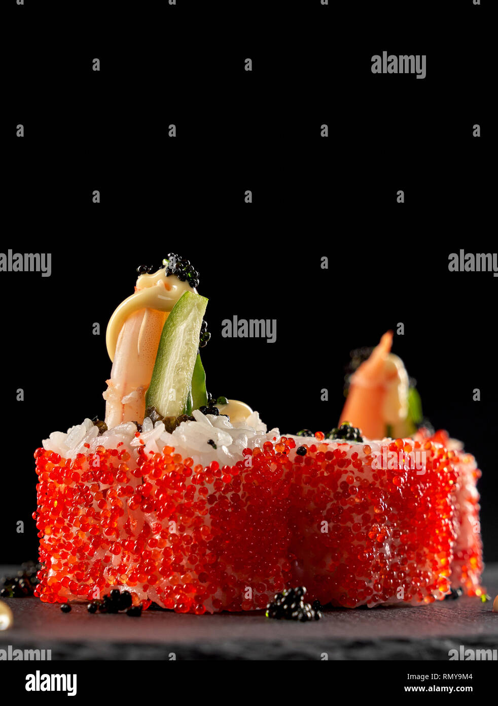 Volcano sushi covered with red flying fish roe. Japanese uramaki rice rolls with shrimp, cucumber and topped with sauce and black caviar. Stock Photo
